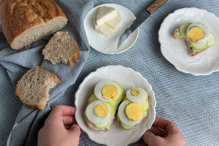 Top view of woman hands preparing healthy homemade sandwiches with vegetables and hard-boiled eggs