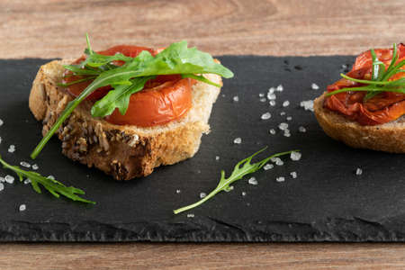 Delicious homemade bruschetta with whole grain bread, grilled tomatoes and fresh arugula. Vegetarian healthy snack, vegan foodの写真素材
