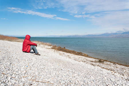 Lonely man sitting on the lakeshore, admiring the nature. Unrecognisable person, wanderlust
