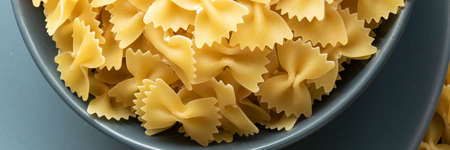 Food background - dry farfalle pasta on grey plate, whole wheat uncooked ingredient, space for text