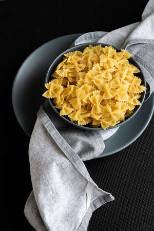 Food background - dry farfalle pasta on grey plate, whole wheat uncooked ingredient, space for text