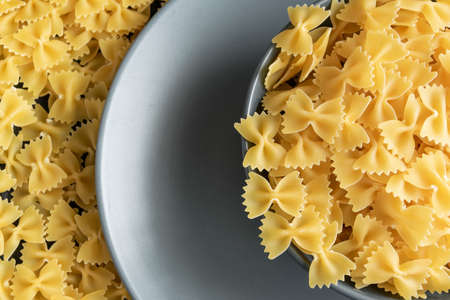 Food background - dry farfalle pasta on grey plate, whole wheat uncooked ingredient, space for text