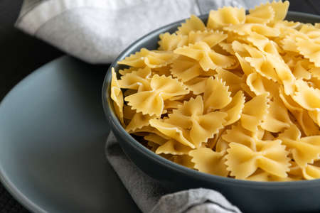 Food background - dry farfalle pasta on grey plate, whole wheat uncooked ingredient, space for textの写真素材