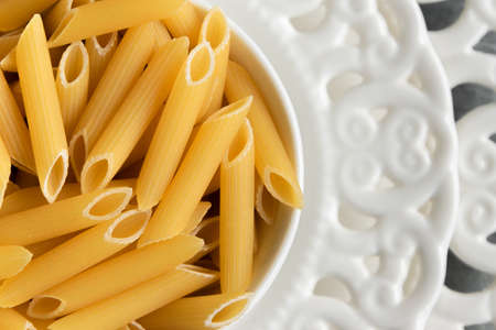 Dry penne pasta on blue white vintage plate, whole wheat uncooked ingredient, space for textの写真素材