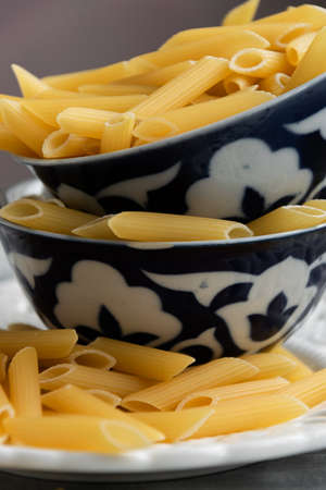 Dry penne pasta on blue vintage plate, whole wheat uncooked ingredient