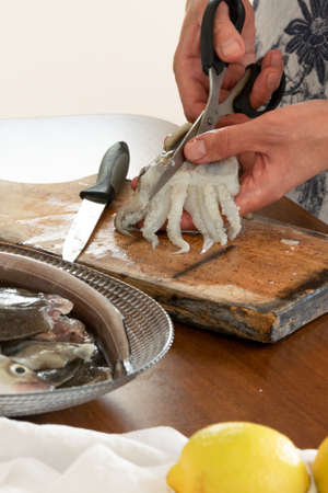Woman cutting cuttlefish on kitchen table, healthy cooking conceptの写真素材