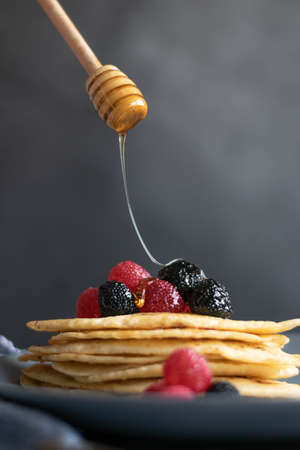 Pouring raw honey over homemade crepes on table, dark food photography
