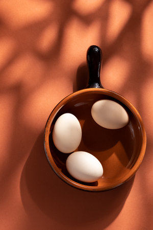 Handmade ceramic plates with home eggs on brown background. Terracotta objects, space for text. Genuine food concept.の写真素材