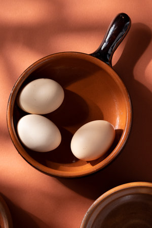 Handmade ceramic plates with home eggs on brown background. Terracotta objects, space for text. Genuine food concept.の写真素材