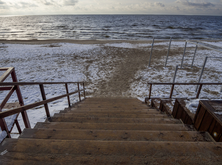 Wooden steps down to the sandy beach in the Baltic Sea on a winter cloudy day at sunset in Klaipeda, Lithuaniaの写真素材