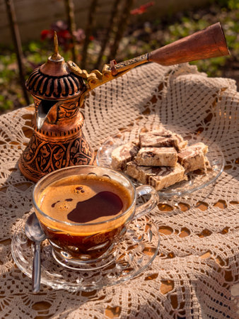 Greek (Turkish) brewed coffee and marble halva on a table with a handmade tablecloth and a copper coffee maker and candy maker on a Sunny dayの写真素材