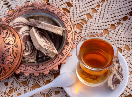 Turkish tea in a glass Cup and marble halva on a table with a handmade tablecloth and candy maker on a Sunny dayの写真素材