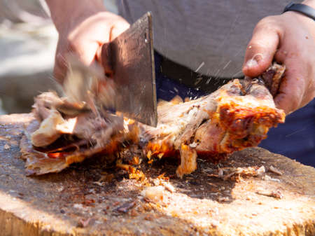 A man is chopping meat with an ax-knife traditional food - goat or lamb on a spit - for the Easter holiday on a wooden block on the Greek island of Greeceの写真素材