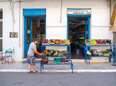 Methana, Peloponnese, Greece. June 2021: A small shop selling fruits and products and a female seller on the street of a resort town in Greece on a summer dayのeditorial素材