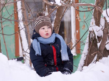 A boy in a knitted hat and with a knitted scarf in winter plays in the snow.の写真素材