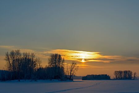 Orange sunset over a snowy plain and trees.の写真素材