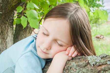 summer outdoor girl child on a tree on a background of leavesの写真素材