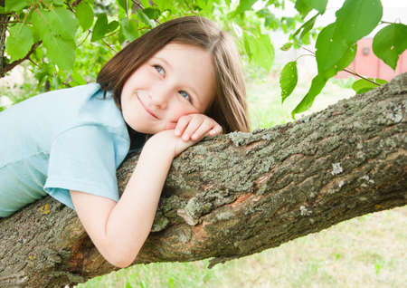 summer outdoor girl child on a tree on a background of leavesの写真素材