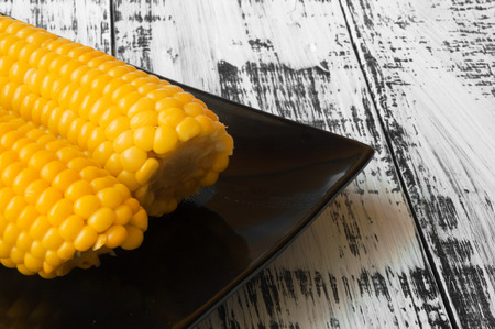 Tasty yellow corn on a black plate on a white wooden backgroundの写真素材