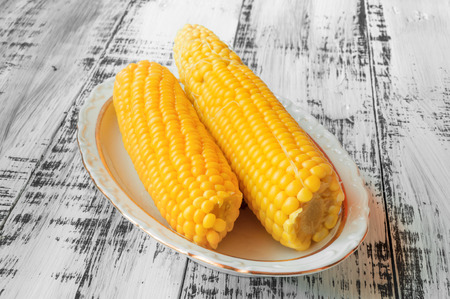 Two delicious yellow corn on a plate on a white wooden backgroundの写真素材