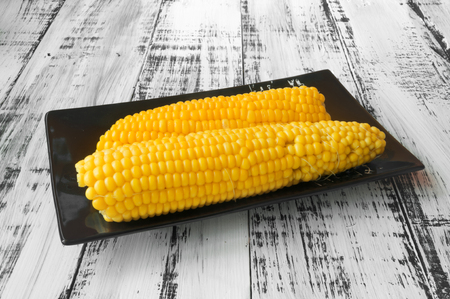 Tasty yellow corn on a black plate on a white wooden backgroundの写真素材