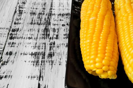 Tasty yellow corn on a black plate on a white wooden backgroundの写真素材