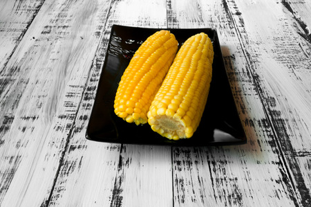 Tasty yellow corn on a black plate on a white wooden backgroundの写真素材