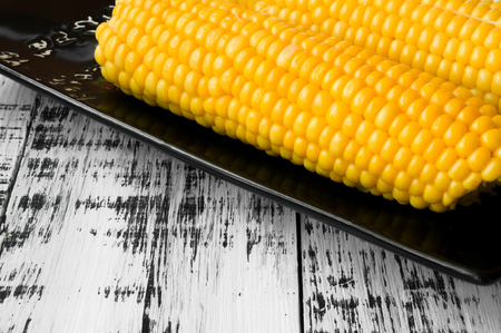 Tasty yellow corn on a black plate on a white wooden backgroundの写真素材
