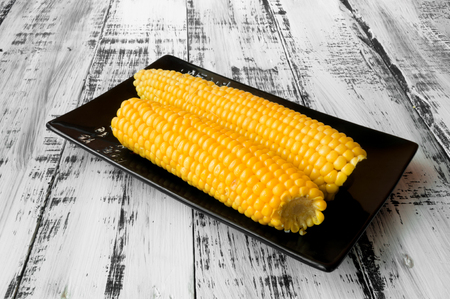 Tasty yellow corn on a black plate on a white wooden backgroundの写真素材