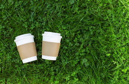 Two white cups of coffee to go on the grass. Place for your text on cups.の写真素材