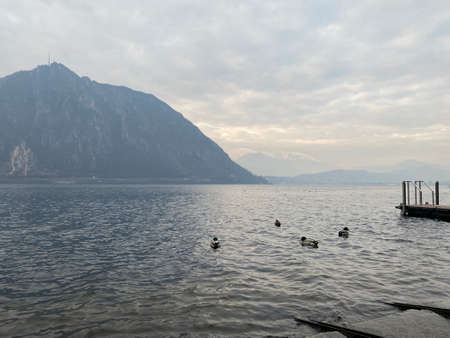 View from the water to Lake Lugano and mountains, Switzerland. Cloudy day, twilightの写真素材
