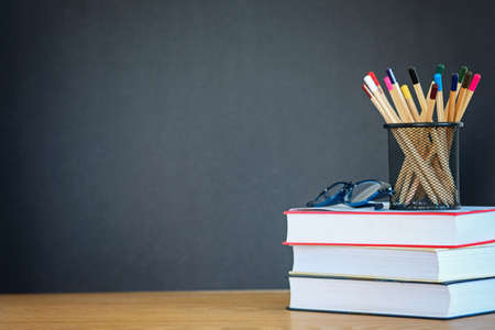 A stack of books, glasses, many pencils in the metal holder on the wooden background of a black school board. The concept of education. Copy space.の写真素材