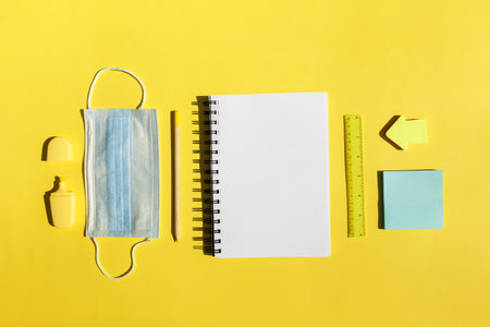 School stationery supplies, medical mask on yellow background social distancing, school reopening after pandemic. New normal concept.Top view copy space,blackboardの写真素材