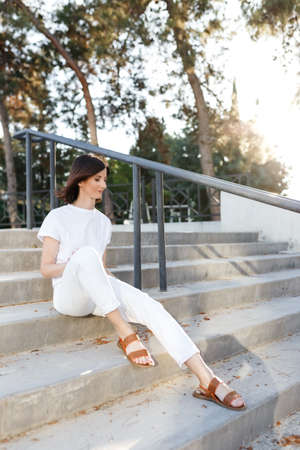 Lifestyle outdoor portrait of beautiful pretty stylish sensual african woman wearing jeans and shirt sitting on stairs and relaxing. Millennial people life and mental health concept.の写真素材