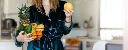 Fresh fruits bucket holded by cropped adult woman with kitchen home background - concept of weight loss and fruit store commerce - healthy eating lifestyle.の写真素材