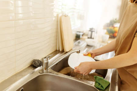 young woman washing dishes in the kitchen sink at home, close up of hands with sponge and soap, housework.の写真素材