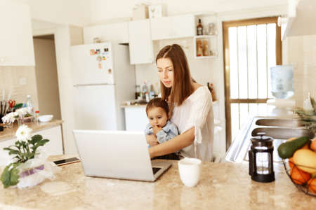 Focused baby boy holding moms hand and trying to walk at home. Full length. Parenthood and childhood concept.の写真素材