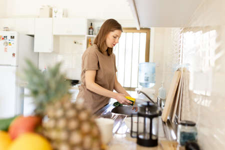 young woman washing dishes in the kitchen sink at home, close up of hands with sponge and soap, housework.の写真素材