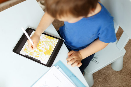 Cute boy in blue t shirt using digital tablet or computer for drawing his picture, using stylus. New...