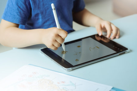 Cute boy in blue t shirt using digital tablet or computer for drawing his picture, using stylus. New...