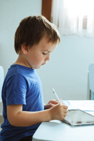 Cute boy in blue t shirt using digital tablet or computer for drawing his picture, using stylus. New...