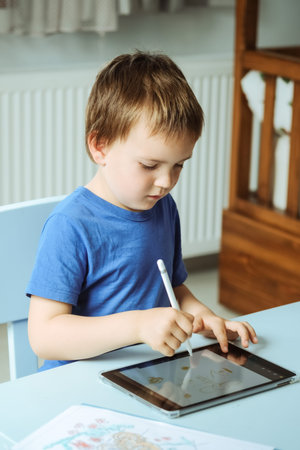 Cute boy in blue t shirt using digital tablet or computer for drawing his picture, using stylus. New...