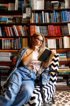 Young beautiful cropped woman standing next to street bricks wall, denim jeans clothes, holding belt satchel purse in shoulder, summer fashion trend, close-up details.の写真素材