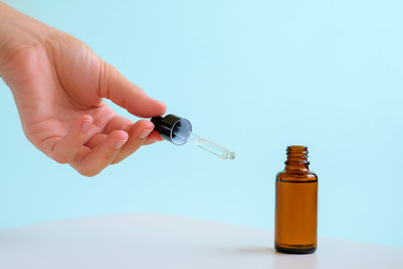 Female hand holds the essential oil falling from the amber glass dropper. Bottle of cosmetic oil...