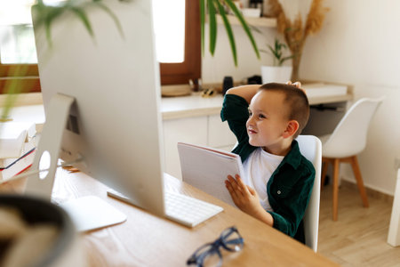 Schoolboy study at desk in his room. Boy use laptop and writing in notebook. Books and tablet on the...
