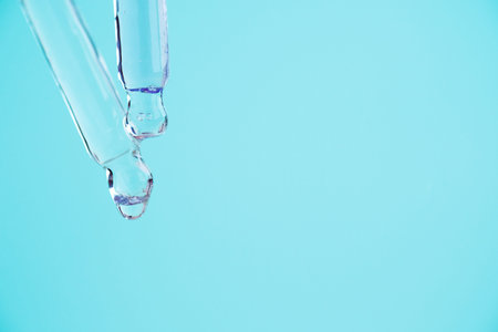 Transparent glass pipettes with a serum liquid dripping on blue background