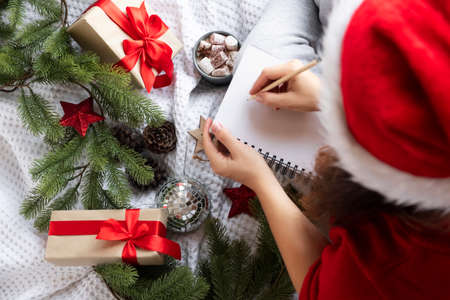 Top view woman writing Christmas wishes in notebook around fir branches and presentsの写真素材