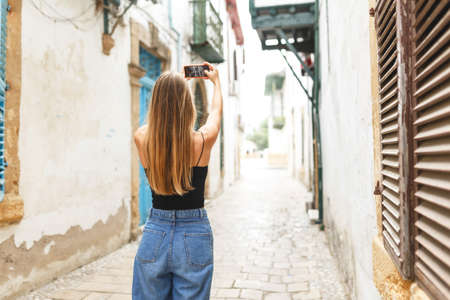 Stylish woman tourist makes a photograph of architecture. The girl is engaged in mobile photography. Street photos on the phone.View from behindの写真素材