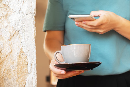 Close shot of woman hands holding mobile phone take photo of cup of coffee foam art in cafe.
