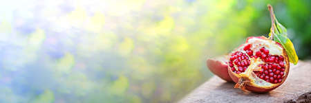 Banner Ripe organic broken pomegranate, cut in half on wooden background. Selective focus, natural green bokeh with sunlightの写真素材